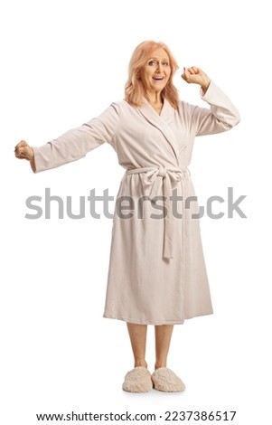 Full lenght shot of a mature woman in a bathrobe stretching and yawning isolated on white background