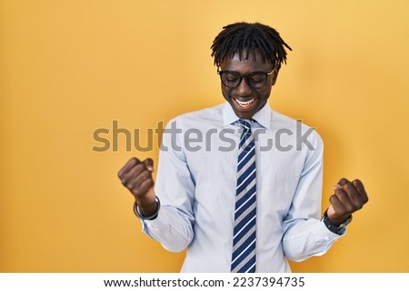 African man with dreadlocks standing over yellow background very happy and excited doing winner gesture with arms raised, smiling and screaming for success. celebration concept.  Royalty-Free Stock Photo #2237394735