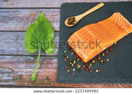 Fresh salmon fillets on black cutting board with herbs and spice