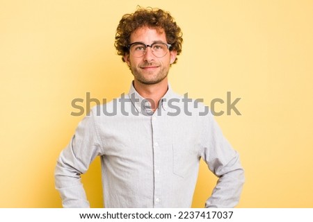 Young smart caucasian man on yellow background confident keeping hands on hips.