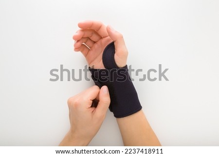 Young adult woman hand putting protective black elastic wrist bandage on white table background. Closeup. Point of view shot. Royalty-Free Stock Photo #2237418911