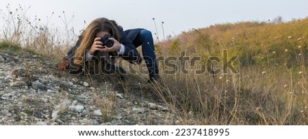 A girl with a camera in her hands in a funny pose makes a frame. Paparazi with a camera in his hands on an outbreak in the mountains.