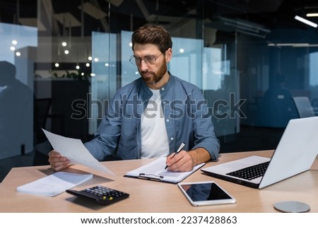Serious and focused financier accountant on paper work inside office, mature man using calculator and laptop for calculating reports and summarizing accounts, businessman at work in casual clothes. Royalty-Free Stock Photo #2237428863