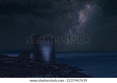 Milky way over sea with a lit up watch tower
