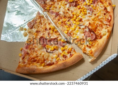 Pieces of pizza with bacon and corn in an open cardboard box, top view
