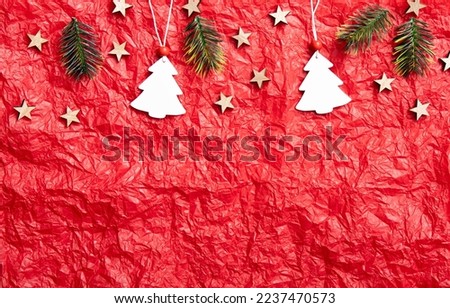 Red crumpled silk paper background with Christmas decorations on upper section, lot of copy space. Studio shot. White Christmas tree shape ornaments hanging, wood stars and spruce branches.