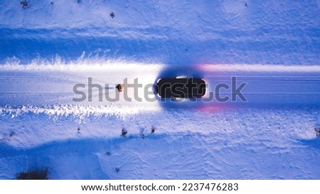 Aerial top view of car on rural area road while headlights are on in winter darkness, bird's eye view of suv vehicle in snowy north lands. Person standing front automobile which lighting the way Royalty-Free Stock Photo #2237476283