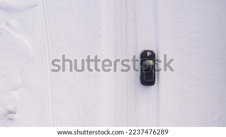 Aerial top view from drone of suv vehicle driving on snowy ice road exploring local landscapes in winter, bird’s eye view of automobile car moving on area in snow