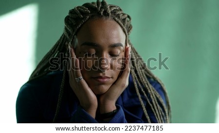One pensive young black woman in contemplation. Thoughtful African American pensive adult girl with dreadlocks closeup face