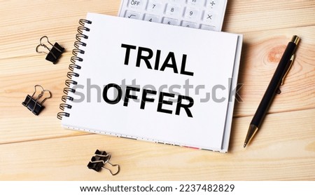 Blank notepad with text TRIAL OFFER, pen, calculator and paper clips on office wooden table.