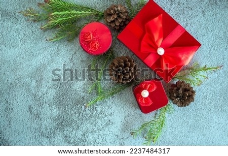 Christmas decoration composition on gray concrete background with a beautiful Red gift box with red ribbon, tree branches, and pine cones