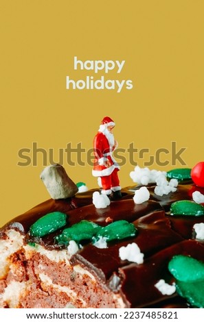 the text happy holidays and a miniature santa standing next to a sack full of gifts, on top of a yule log cake in front of a yellow background
