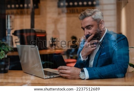 A thoughtful worried mature business man thinking of problem solution while working on a laptop in the office near the window. Royalty-Free Stock Photo #2237512689