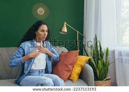 Panic attack woman alone at home scared hispanic woman having trouble breathing sitting on couch in living room. Royalty-Free Stock Photo #2237513193