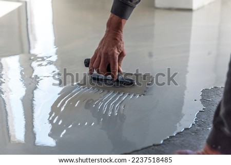 Construction workers are painting the floor using the method self-leveling epoxy.spreading self leveling compound with trowel.Self-leveling epoxy. Leveling with a mixture of cement floors. Royalty-Free Stock Photo #2237518485