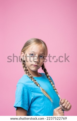 Vertical Studio portrait with pink background of a blonde little girl with braids looking at camera