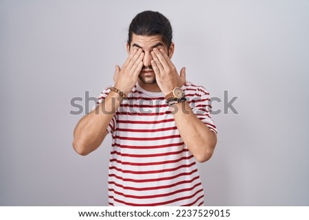 Hispanic man with long hair standing over isolated background rubbing eyes for fatigue and headache, sleepy and tired expression. vision problem 