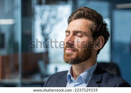 Close-up photo. Portrait of a handsome young man who closed his eyes and rests at the workplace. Sitting relaxed in the office. Royalty-Free Stock Photo #2237529159