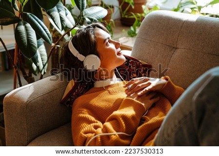 Brunette young woman listening music while resting on couch at home Royalty-Free Stock Photo #2237530313
