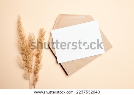 Holiday greeting card mockup with dry grass on beige background, top view, flat lay. White wedding invitation card mock up