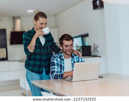 A young married couple is talking to parents, family and friends on a video call via a laptop while sitting in the living room of their modern house