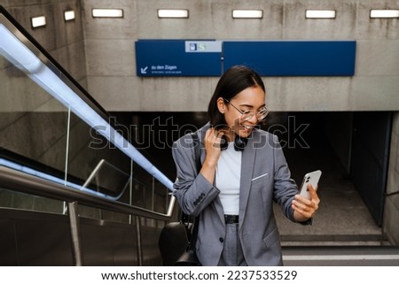 Young joyful asian woman taking selfie on smartphone while standing on city stairs outdoors