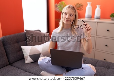 Young blonde woman using laptop with doubt expression at home