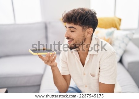 Young arab man talking on the smartphone sitting on sofa at home