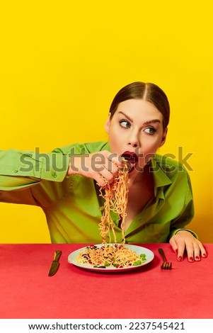 Emotional young girl eating spaghetti, noodles with hands on red tablecloth over yellow background. Vintage style. Food pop art photography. Complementary colors. Copy space for ad, text