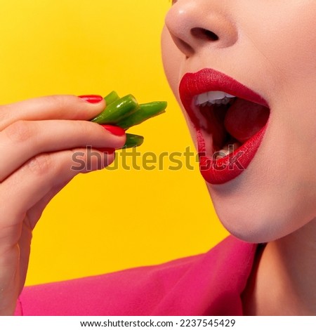 Cropped close up image of young woman, mouth with red lipstick eating boiled green beans over yellow background. Nutrition and health. Food pop art photography. Complementary colors. Copy space for ad