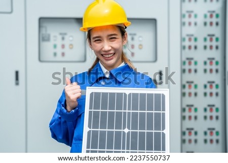 Factory engineer woman standing confidence and holding solar cell panel for renewable energy engineering. manual worker electric al panel background. Concept of smart industry worker operating.