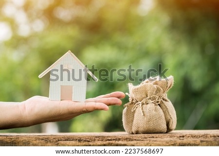 Man hand hold the house under construction present to the money bags put on the wood in the public park. Saving for buy a new home or real estate and loan for plan business investment concept.