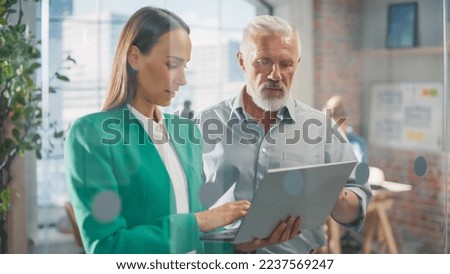 Experienced Senior Engineer Consults Young Designer about a Project in a Creative Office. They Have a Discussion and Work on a Personal Computer to Improve User Experience on Company Website Royalty-Free Stock Photo #2237569247