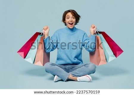 Full body young excited fun woman wears casual clothes hold in hand paper package bags after shopping isolated on plain light pastel blue cyan color background studio Black Friday sale buy day concept