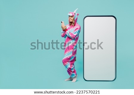 Full body side view young woman wear domestic costume with hoody and animals ears big huge blank screen mobile cell phone with area use smartphone isolated on plain pastel light blue cyan background