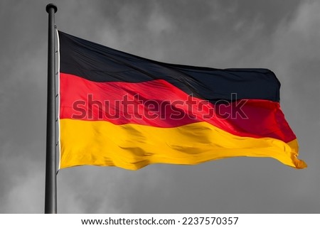 German Flag in black-red-gold colors  as national Symbol of the Bundesrepublik Deutschland. Background in black and white greyscale contrasting the isolated colorful hoisted bannner waving in the wind
