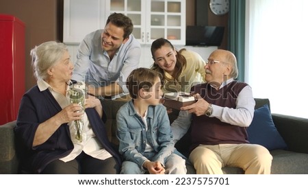 A scene where a young couple gives flowers and a gift box to their elderly parents. The extended family celebrates a birthday, holiday, mother's day or father's day. Happy family portrait.