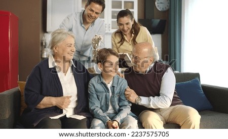 Young couple with children, their son and elderly parents sitting on sofa in living room, chatting together, laughing. Portrait of happy cheerful big family in cozy living room.