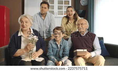 A scene where a young couple gives flowers and a gift box to their elderly parents. The whole family is staring at the empty advertising space to the left of the screen.