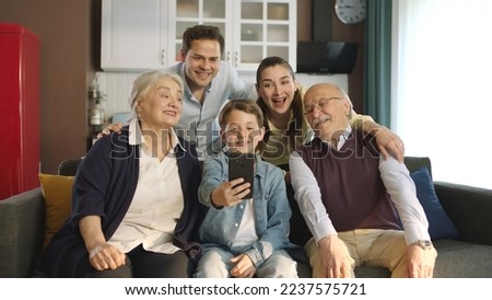 Young couple with children, their son and elderly parents sitting on sofa in living room, taking self portraits together. Portrait of happy cheerful big family smiling at camera in cozy living room. Royalty-Free Stock Photo #2237575721