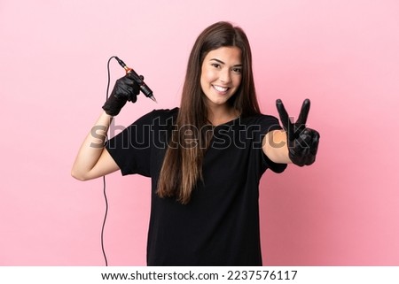 Tattoo artist woman isolated on pink background smiling and showing victory sign