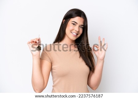 Young Brazilian woman holding home keys isolated on white background showing ok sign with fingers