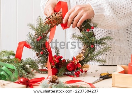 A woman makes and decorates Christmas wreath of spruce branches with red berries colorful ribbons