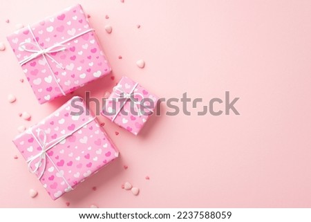 Valentine's Day concept. Top view photo of gift boxes in wrapping paper with heart pattern and sprinkles on isolated pastel pink background with copyspace