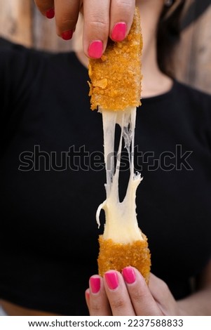Woman stretching fried mozzarella cheese sticks. Royalty-Free Stock Photo #2237588833