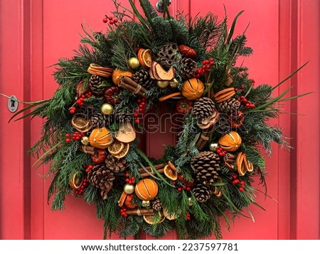 Selective focus of Christmas wreath. Festive christmasy themed winter natural wreath on a pink wooden door, decorated with lotus, pine cones, oranges, vanilla stick. Red berries. Festive mood.