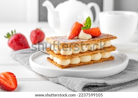 French dessert millefeuille with vanilla cream and fresh strawberries on a white plate on a white wooden background