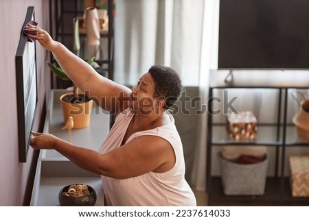 Side view portrait of senior woman cleaning house and dusting wall pictures, copy space