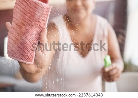 Close up background image of senior woman cleaning glass windows focus on hand holding wipe, copy space