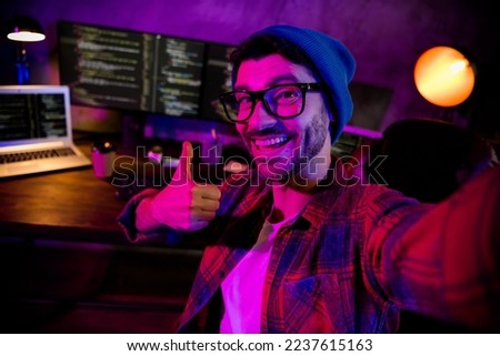 Photo of confident cool coder dressed hat eyewear showing thumb up recording video vlog indoors workplace workstation loft